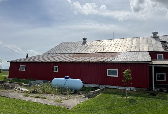 Long red barn with weathered galvanized metal roof panels before replacement
