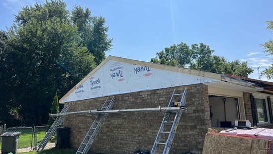 Rebuilt gable end wrapped in housewrap with ladders staged against the brick