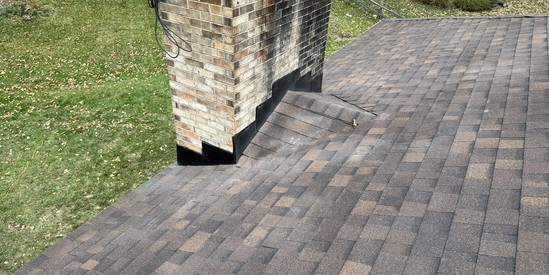 New chimney step flashing installed with fresh shingles around the brick chimney