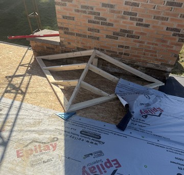 Newly framed chimney cricket with synthetic underlayment around a brick chimney