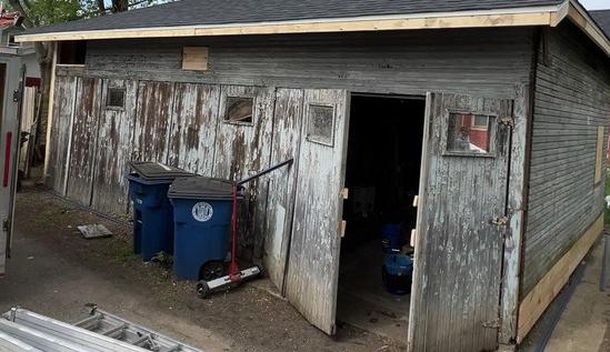 Old weathered detached garage with peeling wood siding before the rebuild